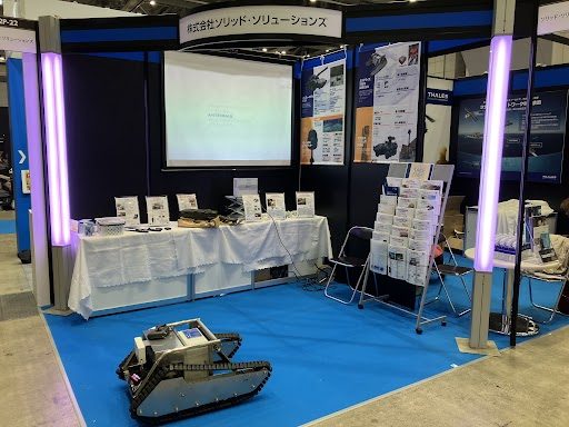 社名を掲げた自社ブースと、床に展示したクローラー型の無人車両